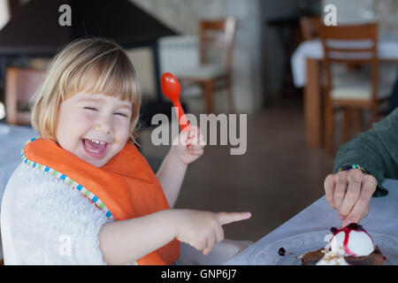 Deux ans drôle et heureux l'enfant avec cuillère en plastique orange et le bib de rire et de pointage du doigt le partage avec une femme pie Banque D'Images