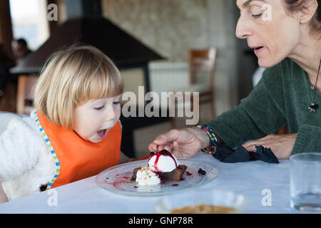 Deux ans avec orange enfant drôle bib surpris face bouche ouverte avec manger expression femme un morceau de gâteau au chocolat avec Banque D'Images