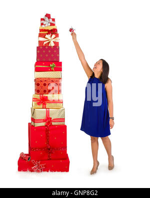 Jeune femme mettant un petit cadeau au sommet d'une énorme pile de cadeaux de Noël Banque D'Images