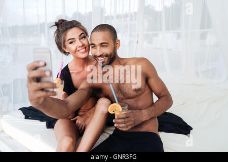 Happy smiling couple multiracial et selfies holding cocktails à la plage Banque D'Images