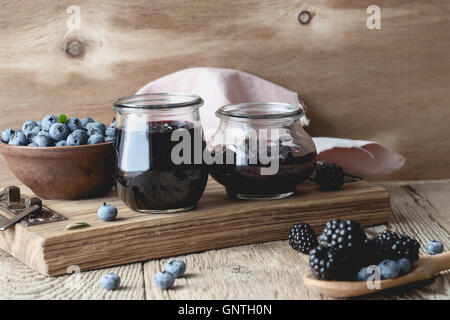 Des bleuets et des mûres de la confiture dans des bocaux en verre et les baies fraîches sur la table rustique en bois Banque D'Images