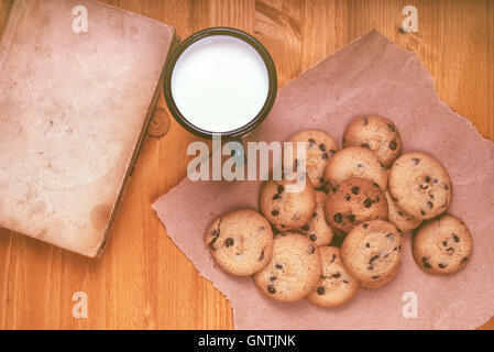 Des cookies aux pépites de chocolat, lait tasse et vintage livre sur table en bois rustique, vue du dessus Banque D'Images