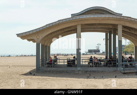 Kiosque / pavillon d'hébergement avec des gens assis sur des bancs à l'ombre sur la plage de Brighton, Brooklyn. Banque D'Images
