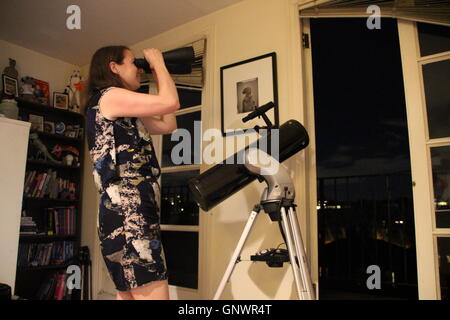 Femme regardant par Celestron jumelles SkyMaster au London night sky debout à côté d'un télescope réflecteur newtonien Banque D'Images