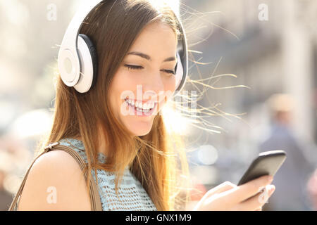 Portrait of a happy girl listening music on line avec des écouteurs sans fil à partir d'un smartphone dans la rue dans une journée ensoleillée d'été Banque D'Images