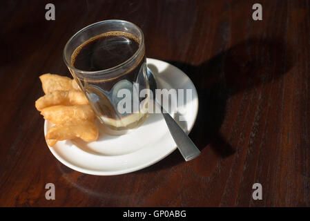 Tradition thaïlandaise café chaud avec le lait condensé sucré dans old style cup, servi avec une pâte frite ou 'patongko' en thaï Banque D'Images