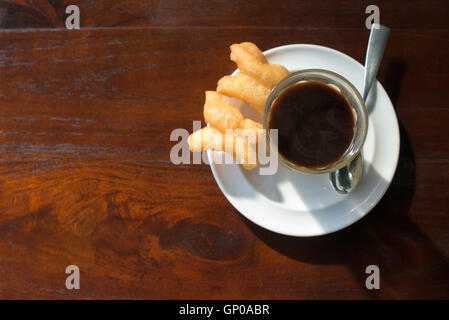 Tradition thaïlandaise café chaud avec le lait condensé sucré dans old style cup, servi avec une pâte frite ou 'patongko' en thaï wor Banque D'Images