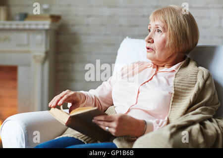 Hauts femme avec livre assis dans un confortable fauteuil Banque D'Images