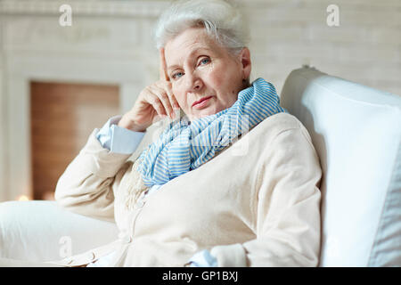 Taille portrait de tranquille et lumineux habillé couleur femme âgée assis confortablement dans blanc coussin chaise appuyée sur sa main un Banque D'Images