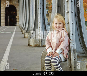 Mettre en place toute l'année et de la hanche à Paris. Portrait of smiling enfant en bonne santé dans le sport vêtements de style assis sur le pont Pont de Bir-Hakeim Banque D'Images