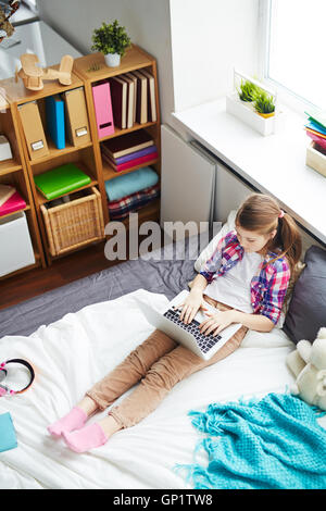 High angle de lycéenne dans sa chambre seule à l'aide d'ordinateur sur lit, temps libre activités enfants Banque D'Images