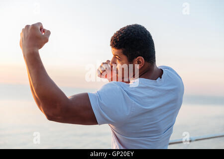 Jeune homme afro-américain musculaire permanent de l'athlète et la pratique de la boxe de l'ombre à l'extérieur Banque D'Images