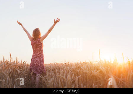 La respiration, la femme à mains levées appréciant le coucher du soleil dans le domaine Banque D'Images