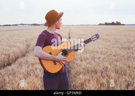 Jeune homme jouant de la guitare dans le domaine au coucher du soleil, l'amour romantique chanson Banque D'Images