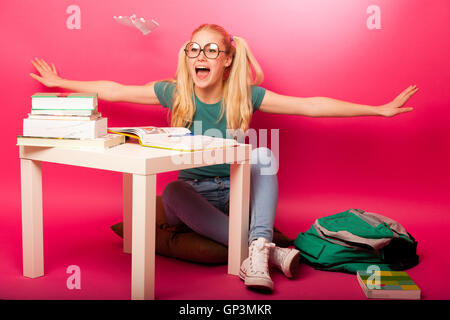 Espiègle, naughty schoolgirl avec de grandes lunettes jouant avec avion en papier alors que devrait étudier. Assis derrière tabe plein de boo Banque D'Images