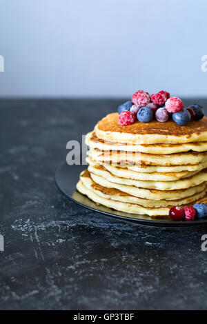 Pile de crêpes aux fruits rouges, noix et miel sur fond sombre Banque D'Images