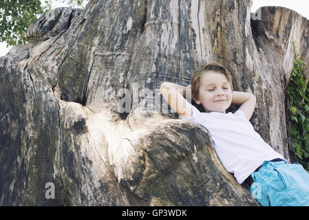 Boy leaning against big tree trunk Banque D'Images