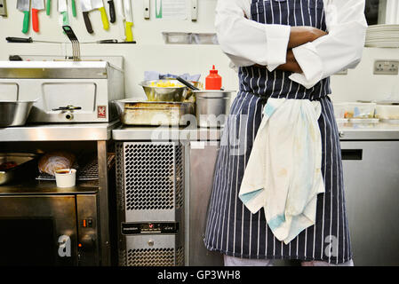 Chef standing in commercial kitchen with arms folded, mid section Banque D'Images