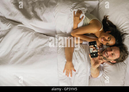 En couple avec le smartphone selfies en position couchée dans le lit Banque D'Images