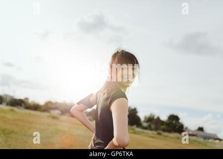 Photo en plein air d'une jeune femme heureuse regardant la caméra et souriant. femme de fitness sur le terrain le matin. Banque D'Images