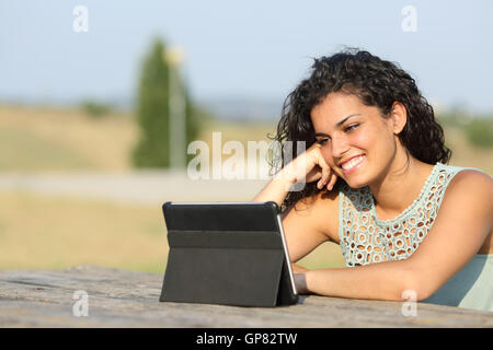 Happy girl regarder des vidéos dans une tablette dans un parc en plein air Banque D'Images