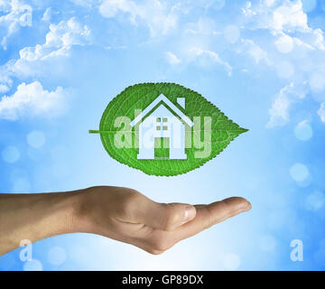 Ouvert main tenant une feuille verte avec une icône en forme de maison à l'intérieur sur un fond de ciel bleu. Eco house concept Banque D'Images