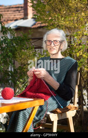 Senior woman knitting avec laine rouge à l'extérieur Banque D'Images