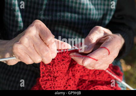 Senior woman knitting mains avec de la laine rouge à l'extérieur Banque D'Images