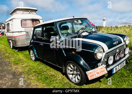 Austin Mini Cooper noir à partir des années 1980 jusqu'en stationnement après le remorquage une très petite caravane. Banque D'Images