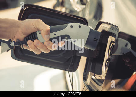 Image couleur de la main d'un homme prêt à charger une voiture électrique. Banque D'Images