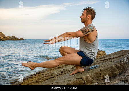 Athletic homme séduisant de l'exercice et l'élaboration avec poids du corps sur la roche par la mer Banque D'Images