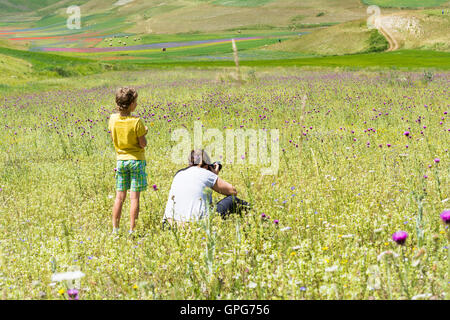 Castelluccio,Italie-juillet 9,2016:Femme et enfant chercher et prendre photograf multicolore de fleurs des champs sur le plateau de Castellu Banque D'Images