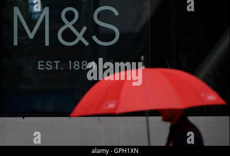 Un homme portant un parapluie marche dernières signalisation au siège social des marques &AMP ; Spencer à Londres, comme la société est de couper autour de 500 emplois à son siège social, selon des rapports. Banque D'Images