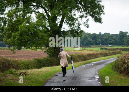 Woman with hat walking avec parapluie sur lane avec arbre Banque D'Images