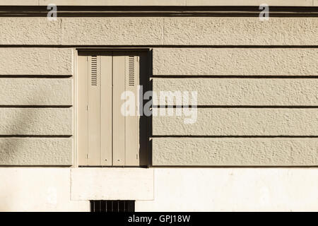 Un mur peint en gris avec des bandes horizontales et une fenêtre avec des volets fermés. Banque D'Images