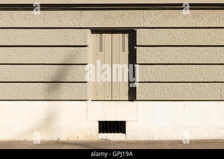 Un mur peint en gris avec des bandes horizontales et une fenêtre avec des volets fermés. Banque D'Images