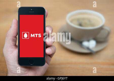 Un homme se penche sur son iPhone qui affiche le logo de l'opérateur de télécommunications MTS, avec une tasse de café (usage éditorial uniquement). Banque D'Images