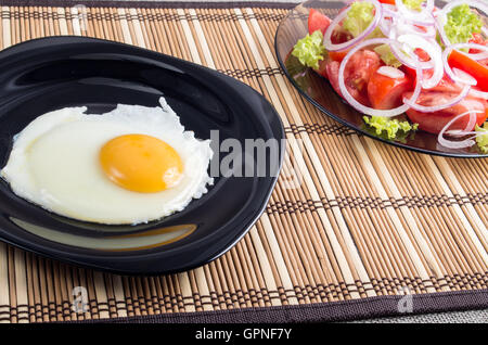 Vue rapprochée sur les petit-déjeuner fait maison d'œuf frit et salade de tomates fraîches sur un tapis à rayures Banque D'Images