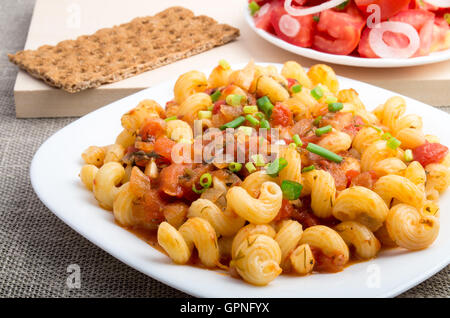 Les pâtes cuites à l'étuvée avec cavatappi sauce légumes et les poireaux servi avec une salade de tomates et pain de seigle sur le textile backgroun Banque D'Images