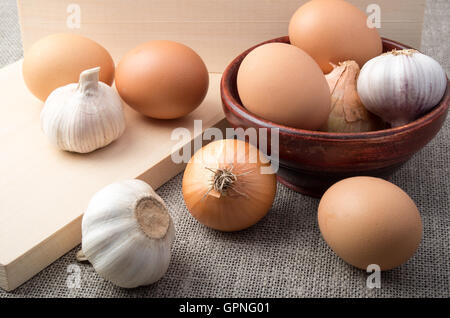 Ingrédients pour la cuisson - les oeufs crus, les oignons et l'ail sur un fond de toile de jute dans un style vintage Banque D'Images