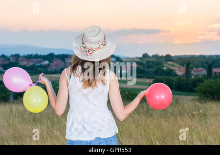 Jeune femme tenant des ballons et à la recherche au coucher du soleil Banque D'Images