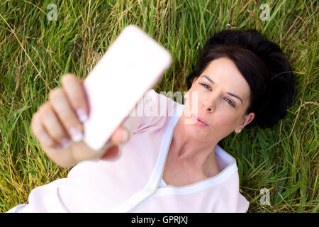 Femme couchée sur l'herbe en prenant un selfies Banque D'Images