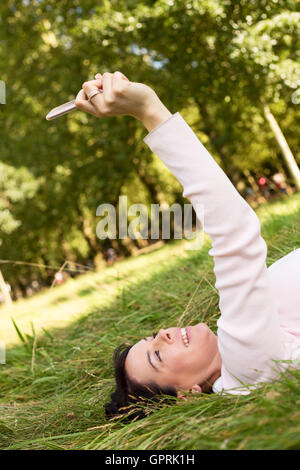 Jeune femme allongée sur l'herbe en prenant un selfies Banque D'Images