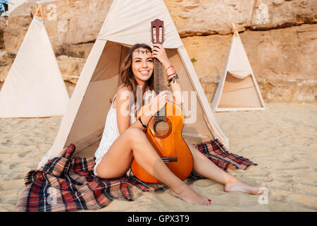 Smiling young woman posing with hippie de la guitare à la plage tente Banque D'Images