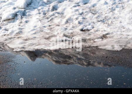 Gros tas de neige fondre sur asphalte avec reflection in puddle Banque D'Images