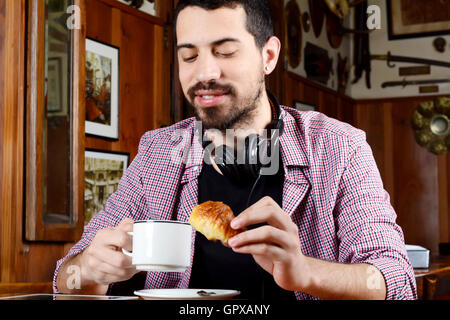 Portrait de jeune homme latin de boire du café avec un casque et tablette numérique dans un café. À l'intérieur. Banque D'Images