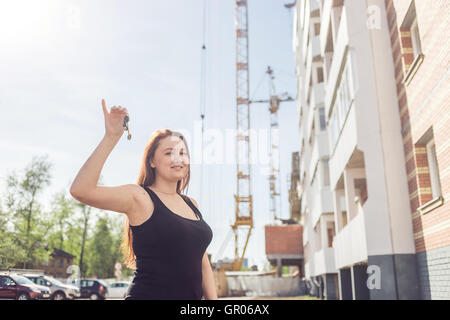 Beautiful smiling woman montrant sa nouvelle maison clefs dans le contexte d'une maison en construction Banque D'Images