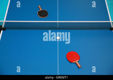 Pour raquettes de tennis de table bleu de couleur rouge et noir et d'une balle sur une table de ping-pong, vue de dessus Banque D'Images