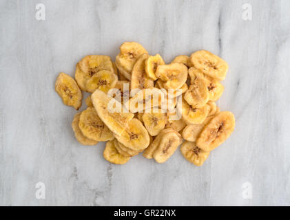 Vue de dessus de banane déshydratée jetons sur une planche à découper en marbre gris. Banque D'Images