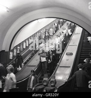 Années 1950, historique des personnes utilisant les escaliers mécaniques en bois dans le métro de Londres. Banque D'Images